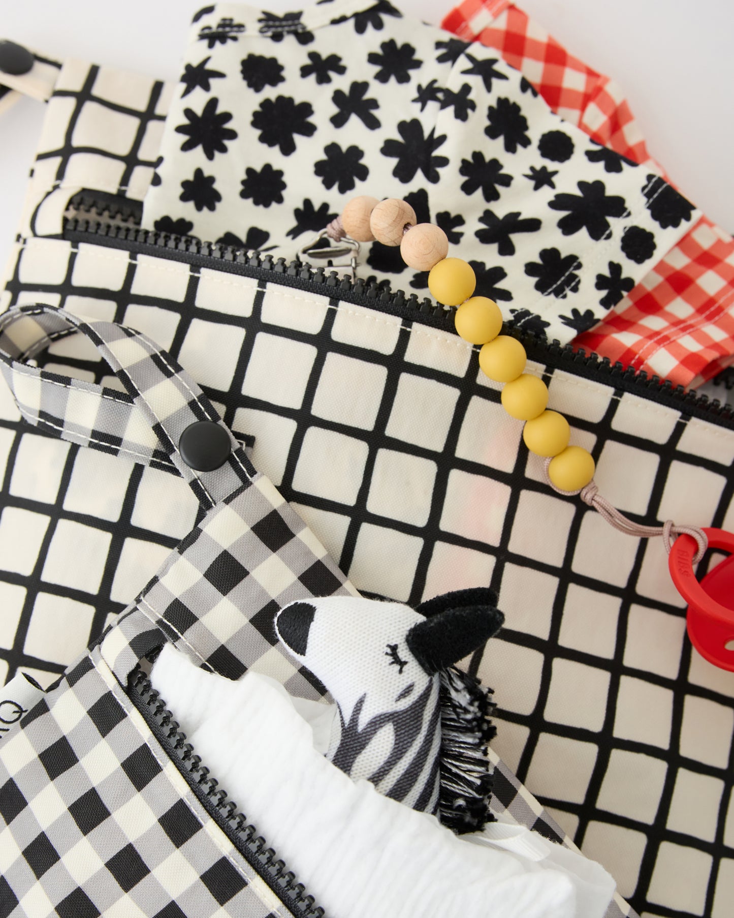 Wet/Dry Bag Set in Black Grid with diapers, zebra lovey, pacifier and onesies peeking out of the bags, on a beige background.