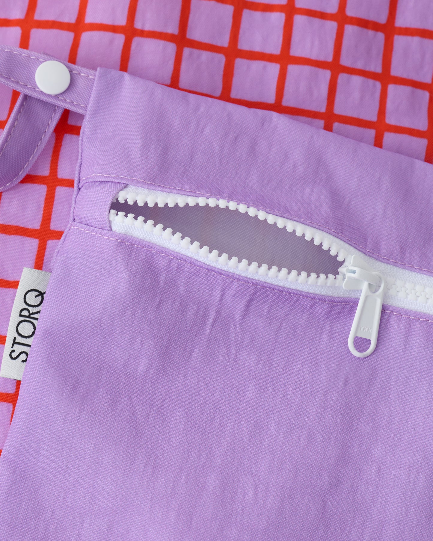 Close up of the zippers and snap loop of the Wet/Dry Bag Set in Orchid Grid on a beige background.