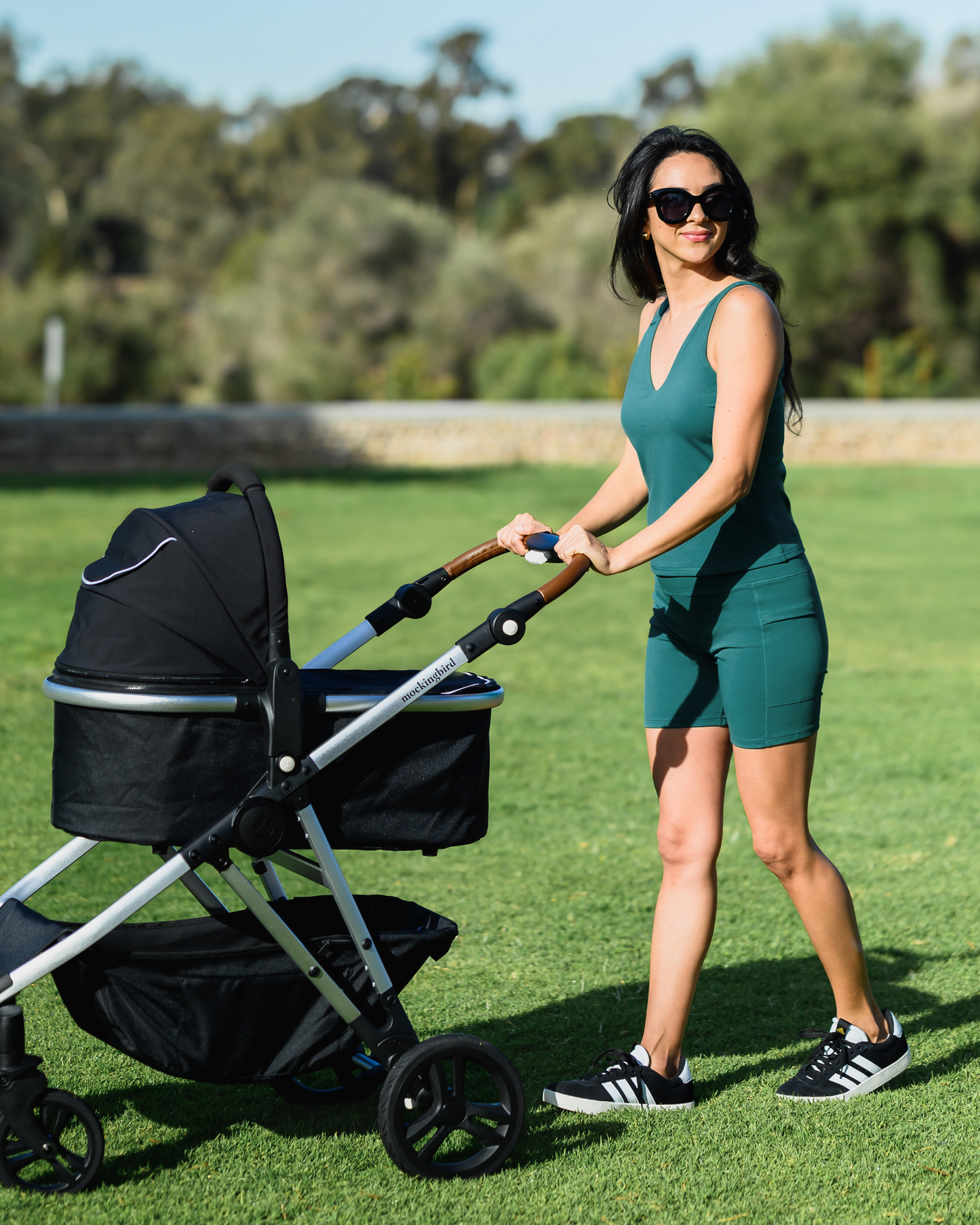 Model pushing baby stroller while wearing the Stevie Active Postpartum Bike Short in Teal with matching Wren Active V-Neck Nursing Tank Top