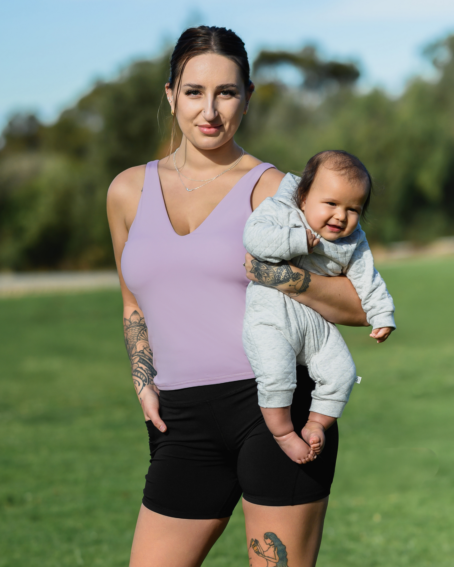 Model holding baby while wearing the Wren Active V-neck Nursing Tank Top in Lavender Mist with matching Stevie Active Postpartum Bike Short @model_info:Anna is wearing a Medium.