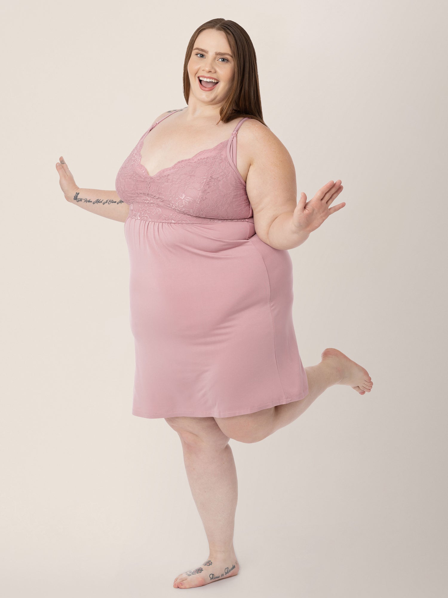 Model wearing the Lucille Maternity & Nursing Nightgown in Vintage Pink standing on one leg and smiling. @model_info:Hayley is 5'7" and wearing a 1X.