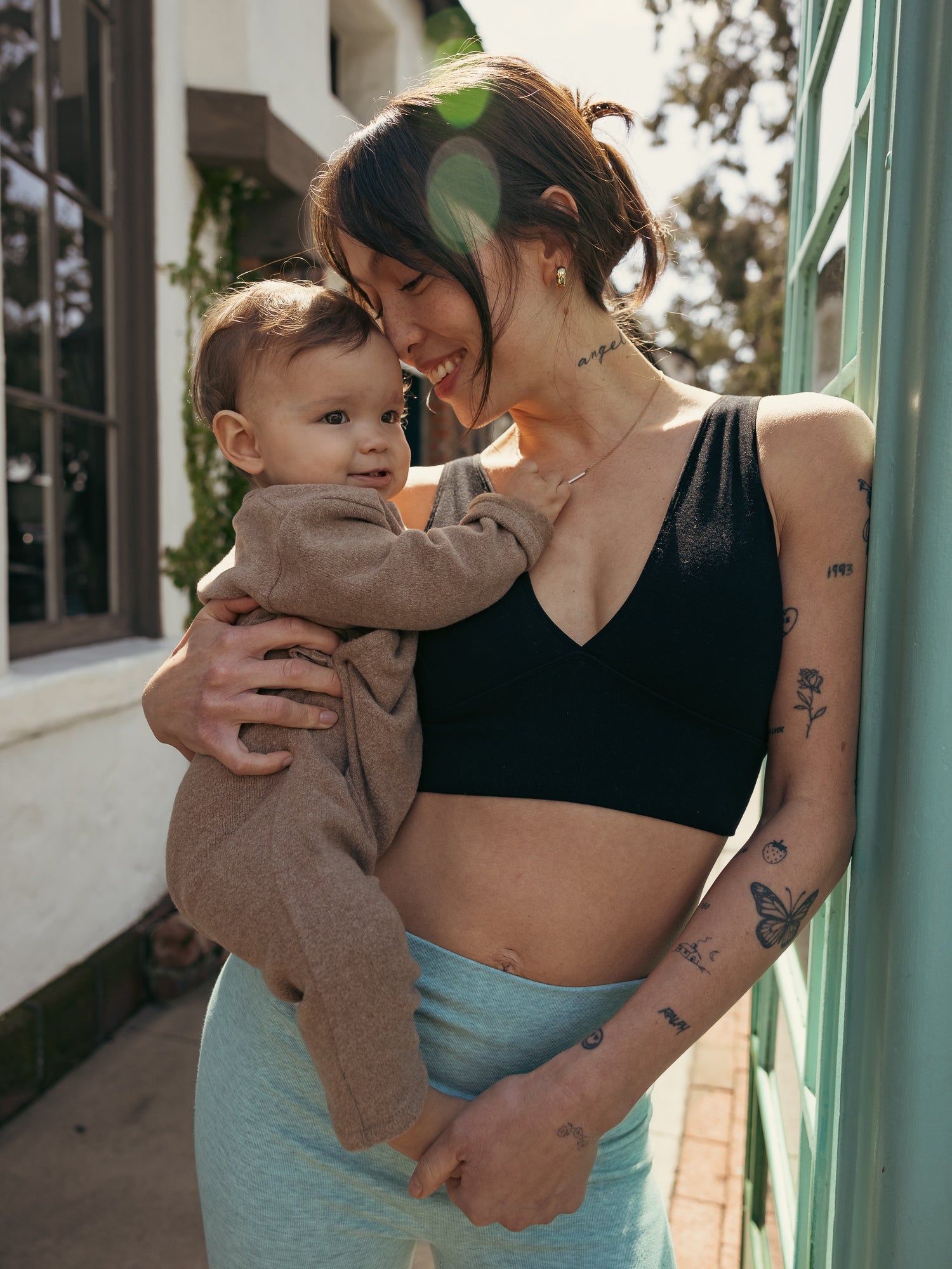 Model wearing the Sublime Maternity & Nursing Plunge Bra in Black paired with the Sublime Bamboo Bike Shorts in Dusty Blue Green. She is holding her baby. @model_info:Lyn is wearing a Small.