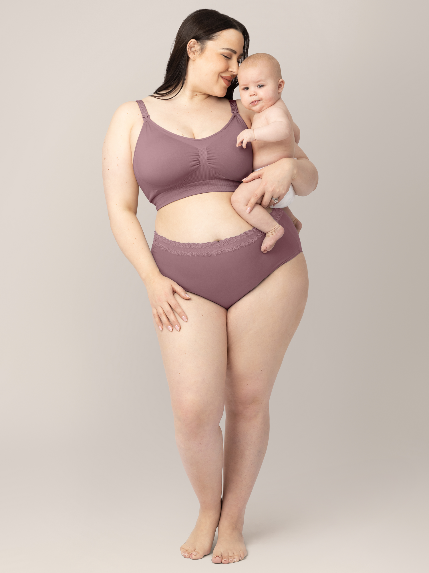 Model holding her baby while wearing the High Waisted Postpartum underwear in Dusty Hues.  @model_info:Rachel is wearing an X-Large.