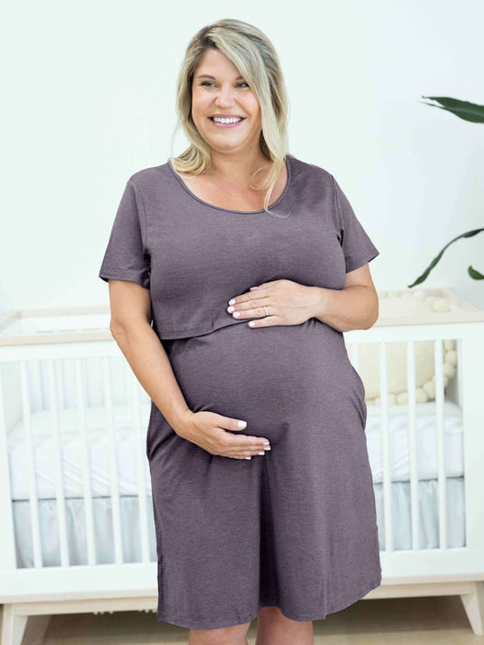 Model wearing the Eleanora Bamboo Maternity & Nursing Dress in Heathered granite, holding her baby bump in front of a crib. @model_info:Katie is 5'2" and wearing a 1X.