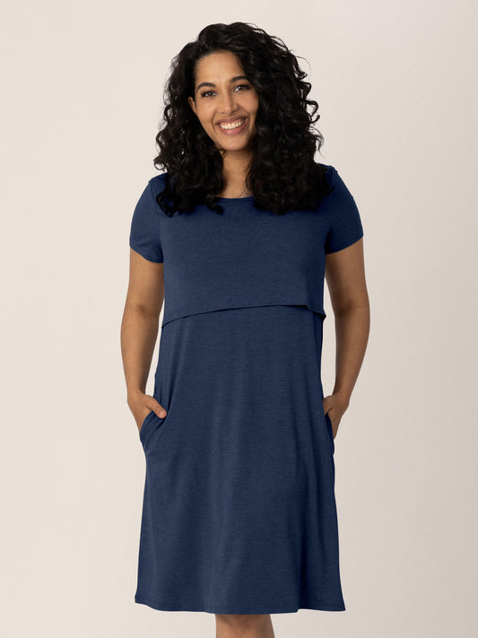 Model standing with her hands in her pockets while wearing the Eleanora Bamboo Maternity & Nursing Dress in Navy Heather. @model_info:Zakeeya is wearing a Small.