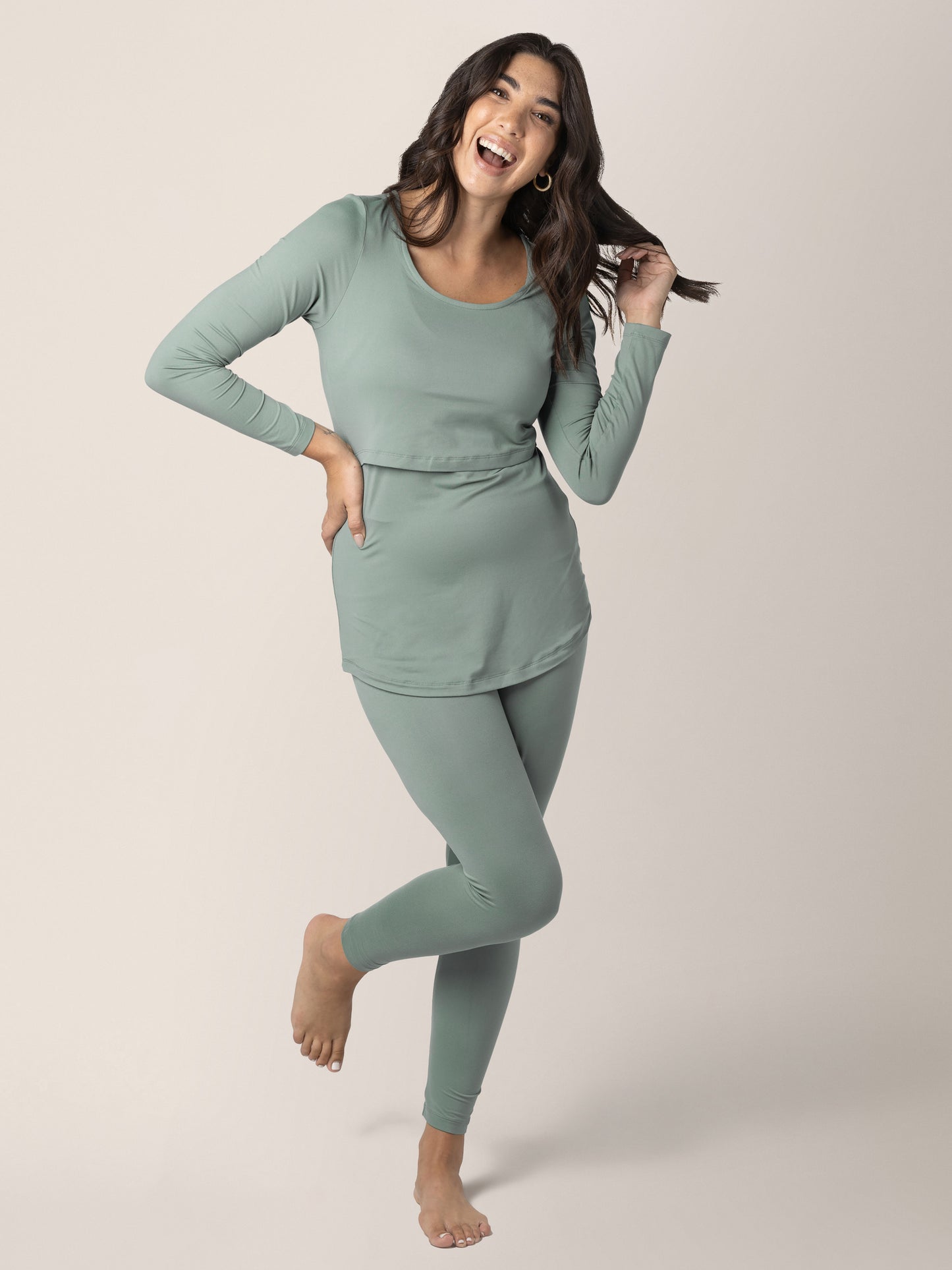 Model standing on one leg playing with her hair while wearing the Jane Nursing Pajama Set in Sage @model_info:Alexis is 5'10" and wearing a Medium.