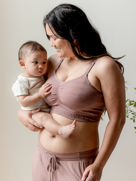 Model holding her baby while wearing the Sublime® Hands-Free Pumping & Nursing Bra in Twilight @model_info:Binc is wearing a Medium Busty.