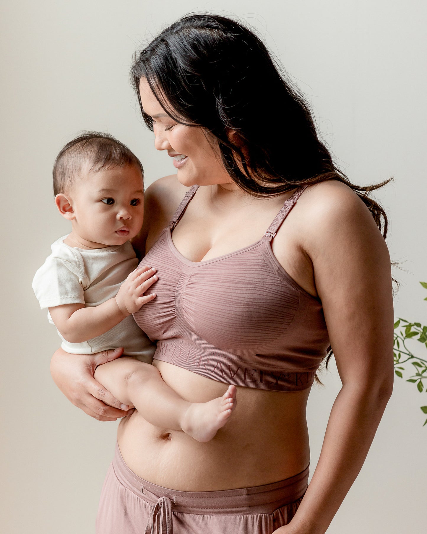 Model holding her baby while wearing the Sublime® Hands-Free Pumping & Nursing Bra in Twilight @model_info:Binc is wearing a Medium Busty.