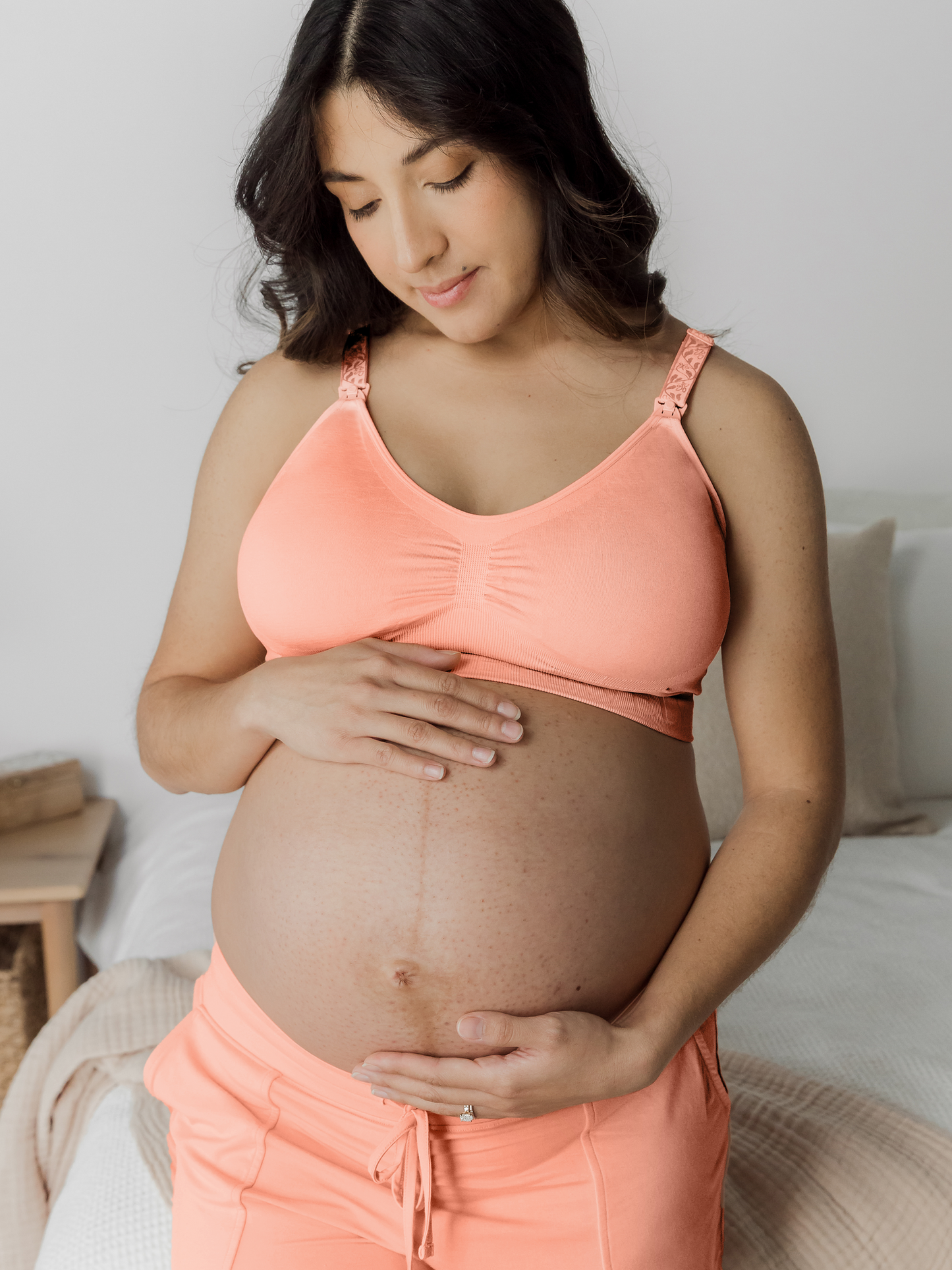 Pregnant model wearing the Simply Sublime® Nursing Bra in Vintage Coral holding her pregnant belly. @model_info: Patty is wearing a Medium Busty.