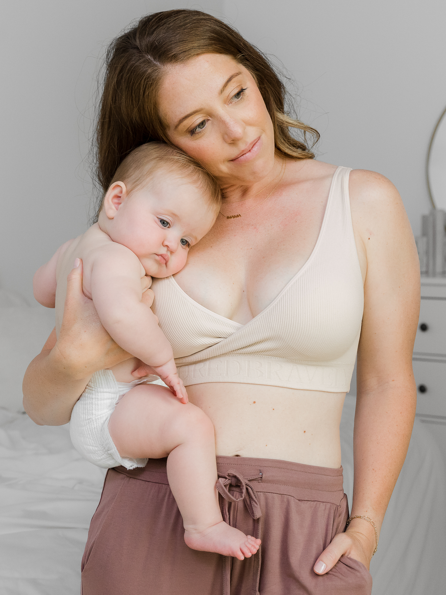 Model holding her baby while wearing the Sublime® Adjustable Crossover Nursing & Lounge Bra in Stone @model_info:Ashley is wearing a Small.