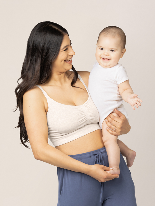 Model holding her baby while wearing the Sublime® Bamboo Hands-Free Pumping Lounge & Sleep Bra in Oatmeal Heather @model_info:Nohely is wearing a Medium Regular.