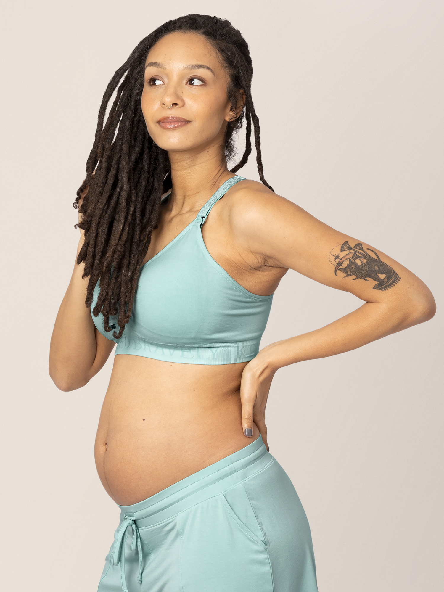 Pregnant model with her hand on her hip and in her hair wearing the Sublime® Hands-Free Pumping & Nursing Sports Bra in Dusty Blue Green. 