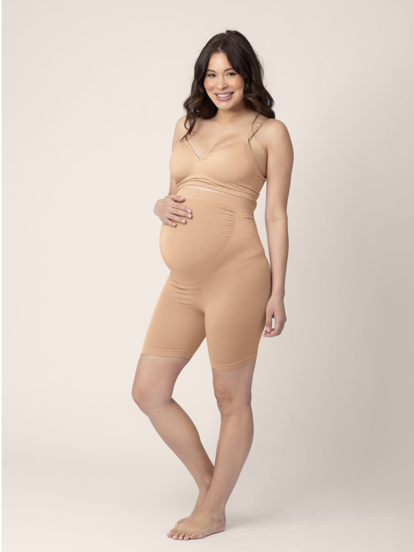 Pregnant model wearing the Seamless Bamboo Maternity Thigh Savers in Beige with her hand on her stomach.@model_info:Vanessa is wearing a Small.