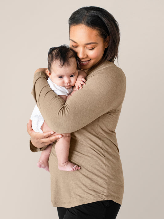Model wearing the Bamboo Maternity & Nursing Long Sleeve T-shirt in Wheat holding her baby against her chest. @model_info:Janalyn is wearing a Medium.
