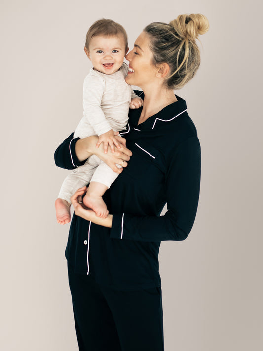 Model wearing the Clea Bamboo Long Sleeve Pajama Set in Black holding her baby on her hip. @model_info:Karin is 5'9" and wearing a Medium.