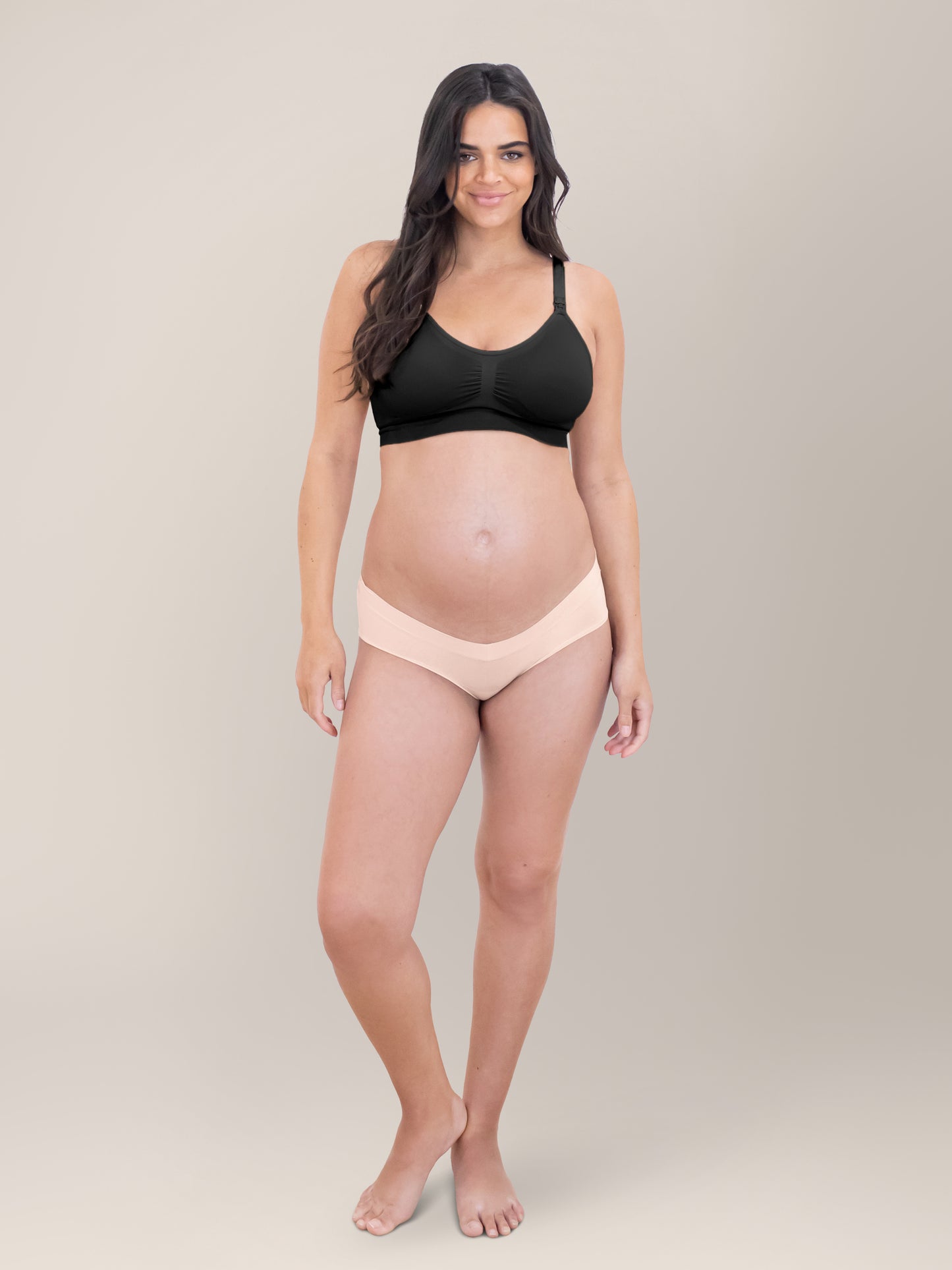 Model standing in front of a grey background  with her hands at her sides wearing the Grow with Me™ Maternity & Postpartum Hipster in Soft Pink. 