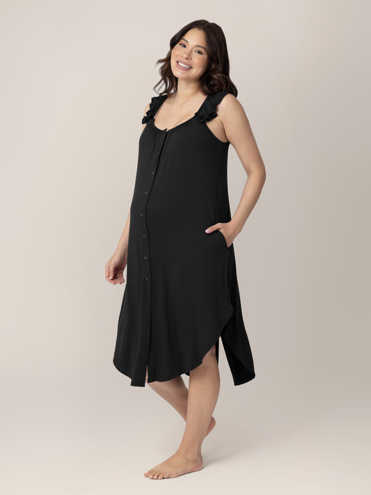 Model wearing the Ruffle Strap Labor & Delivery Gown in Black with her hand in the pocket smiling at the camera. @model_info:Vanessa is 5'8" and wearing a XS/S.