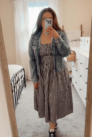 Rotating video of woman wearing Gracie Poplin Nursing Midi Dress in Black & White Gingham with a jean jacket, displaying easy nursing access with hidden zippers, in a light filled bedroom.