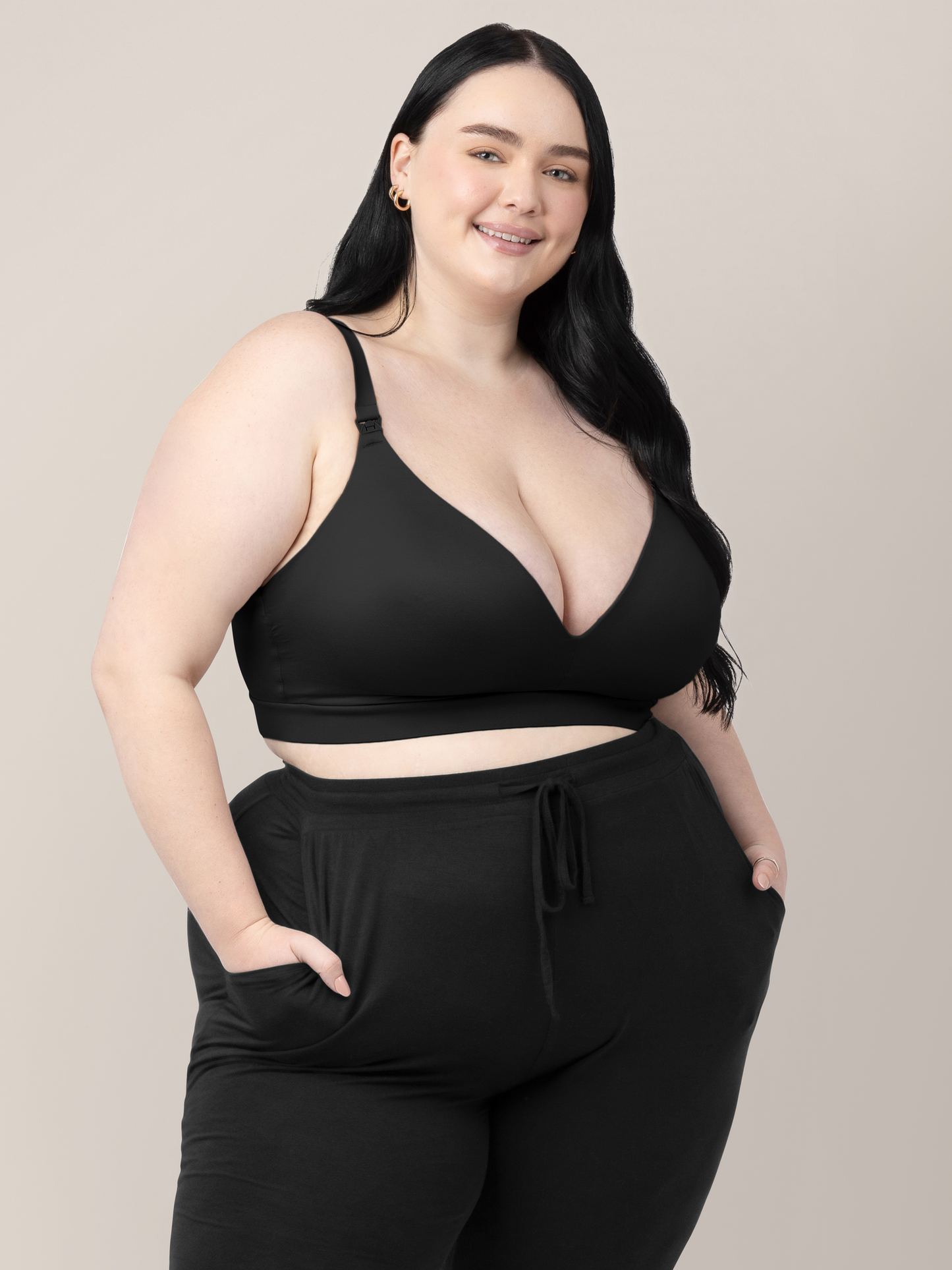 Model wearing the Minimalist Hands-Free Pumping & Nursing Bra in Black with her hands in her pockets. @model_info:Kenna is wearing a 1X Busty.