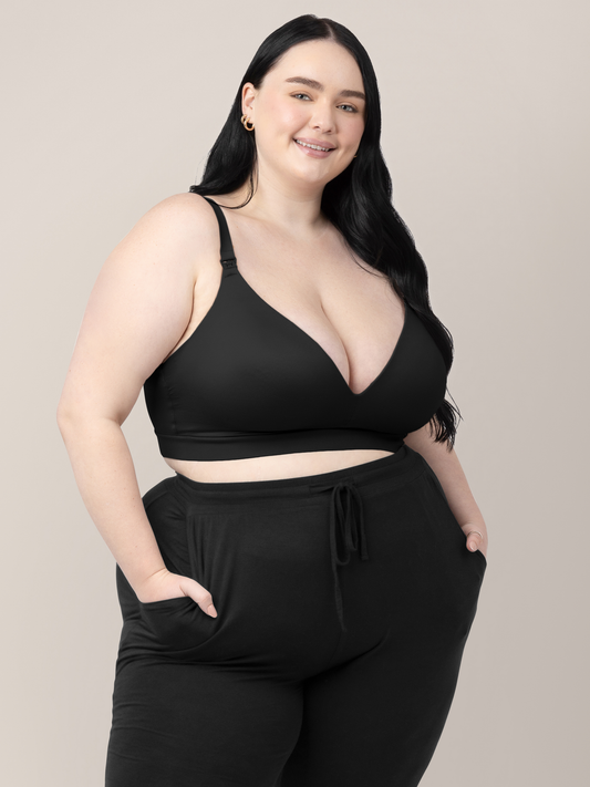 Model wearing the Minimalist Hands-Free Pumping & Nursing Bra in Black with her hands in her pockets. @model_info:Kenna is wearing a 1X Busty.