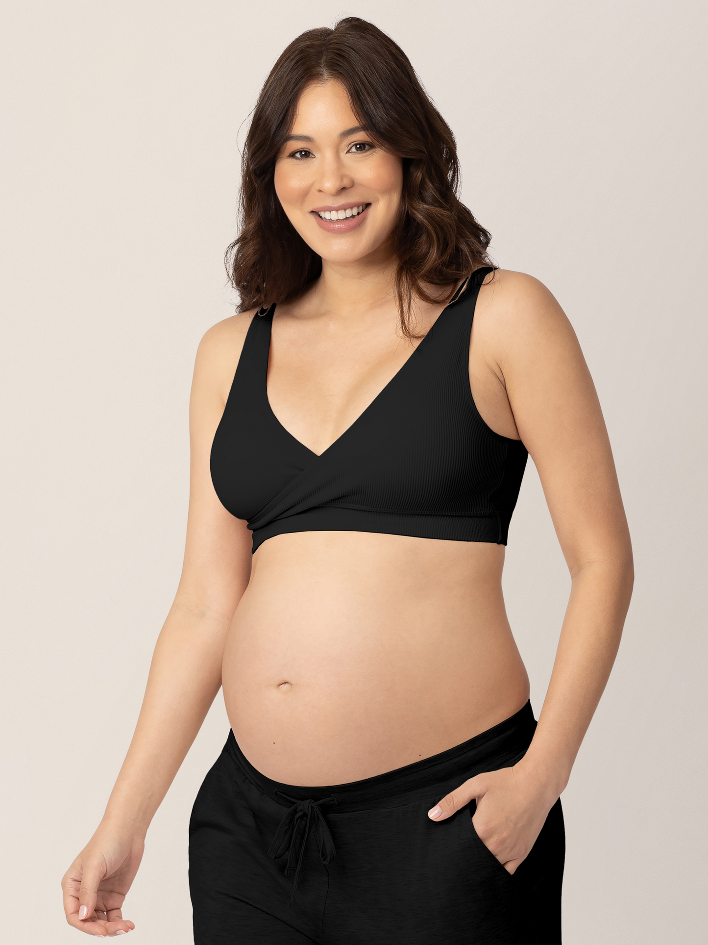 Pregnant Model wearing the Sublime® Adjustable Crossover Nursing & Lounge Bra in Black with her hand in her pocket. 
