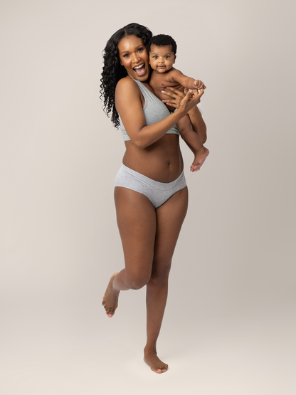 Model wearing the  Bamboo Maternity & Postpartum Hipster in Grey Heather with her baby on her hip smiling. @model_info:Rashé is wearing a Medium.