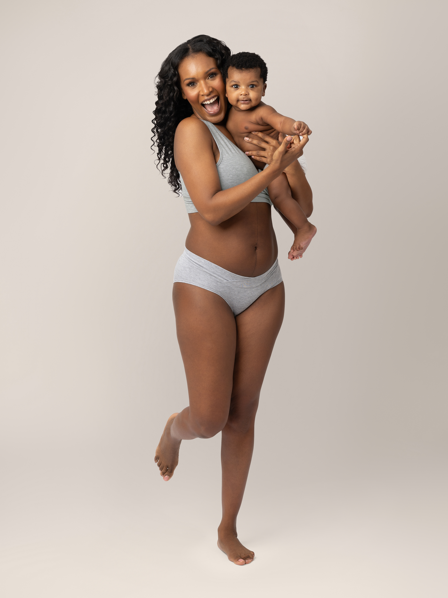 Model wearing the  Bamboo Maternity & Postpartum Hipster in Grey Heather with her baby on her hip smiling. 