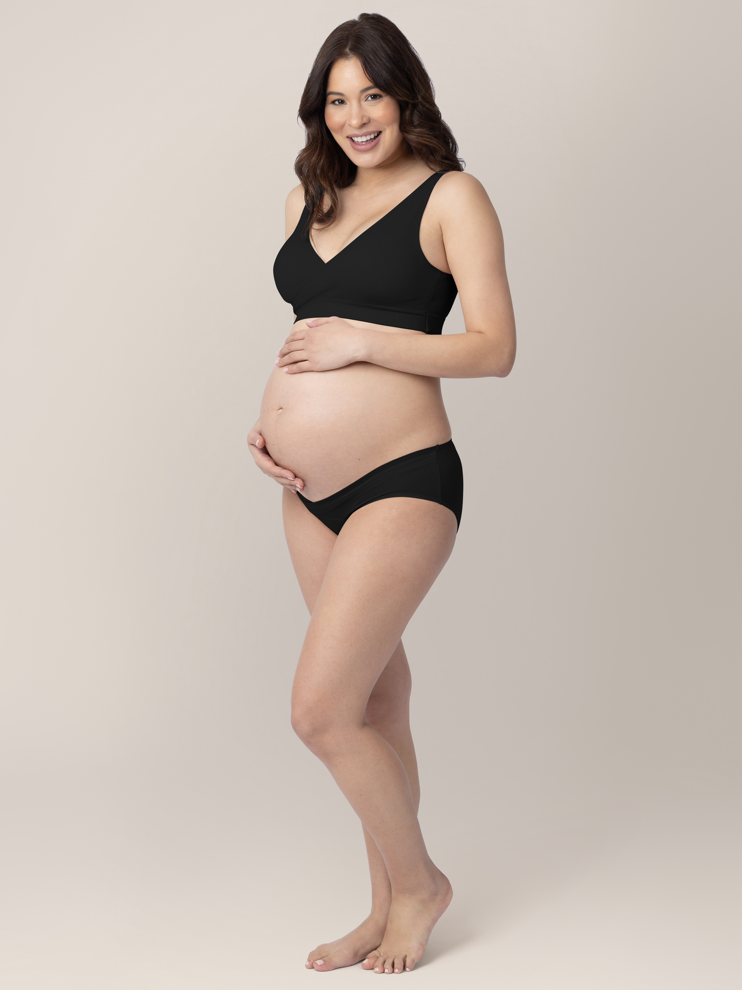 Pregnant model wearing the Under-the-Bump Bikini Underwear in Neutrals with her hands on her stomach. @model_info:Vanessa is wearing a Small.