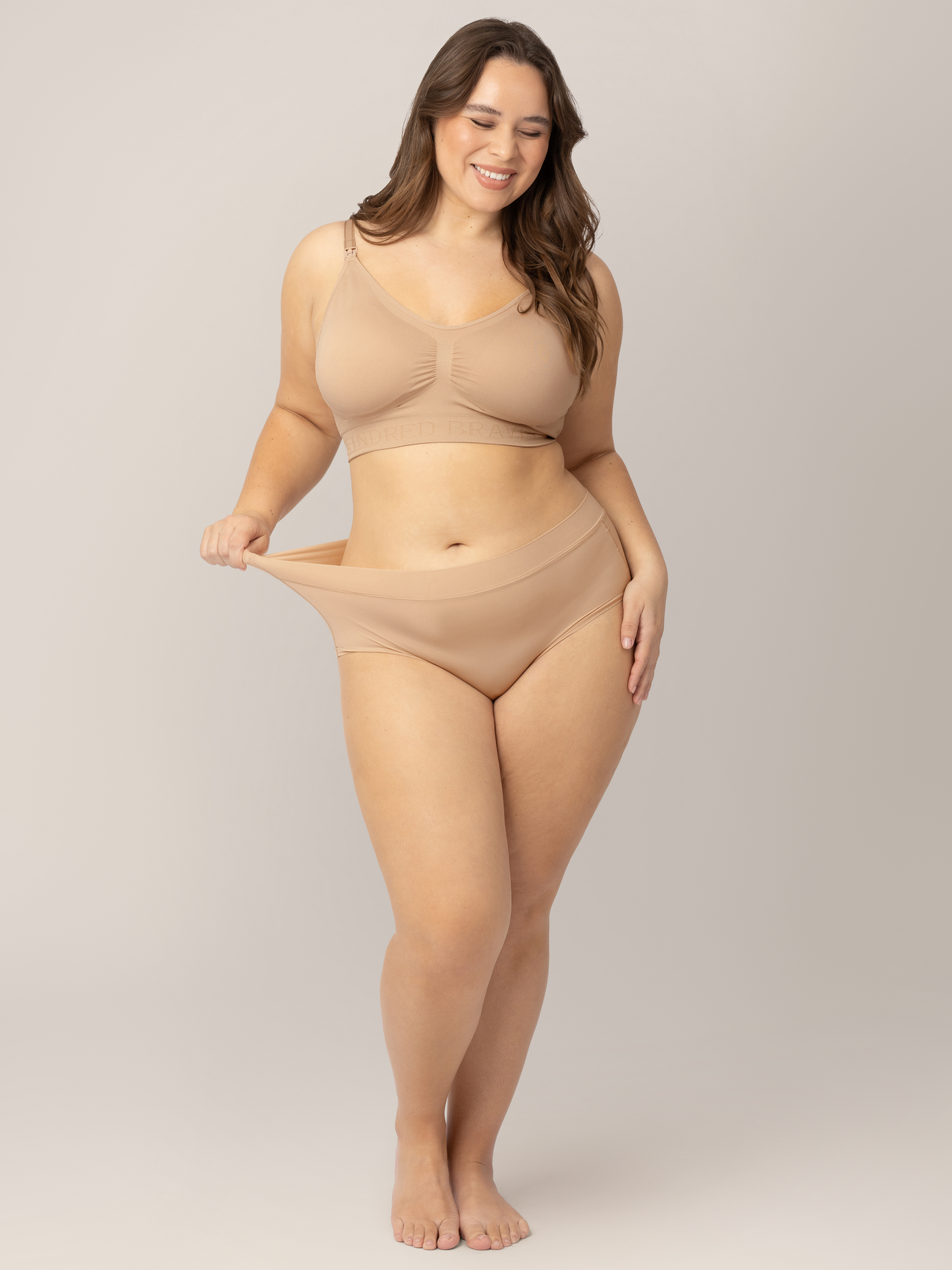 Model tugging on the waistband of her Grow with Me™ Maternity & Postpartum Brief in Beige