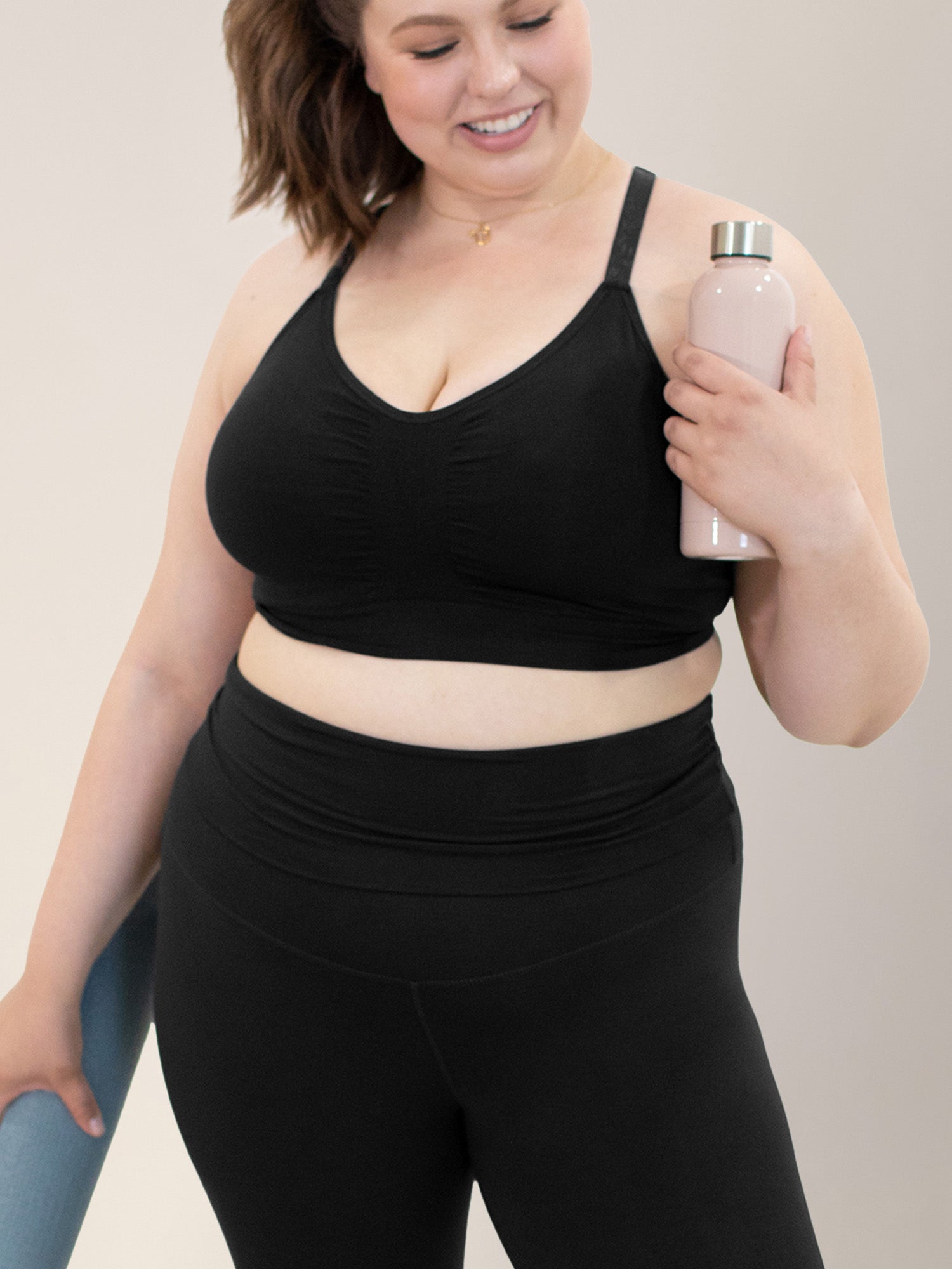 Model holding a light pink metal water bottle and blue yoga mat while wearing the Diana Sublime® Sports Bra in Black