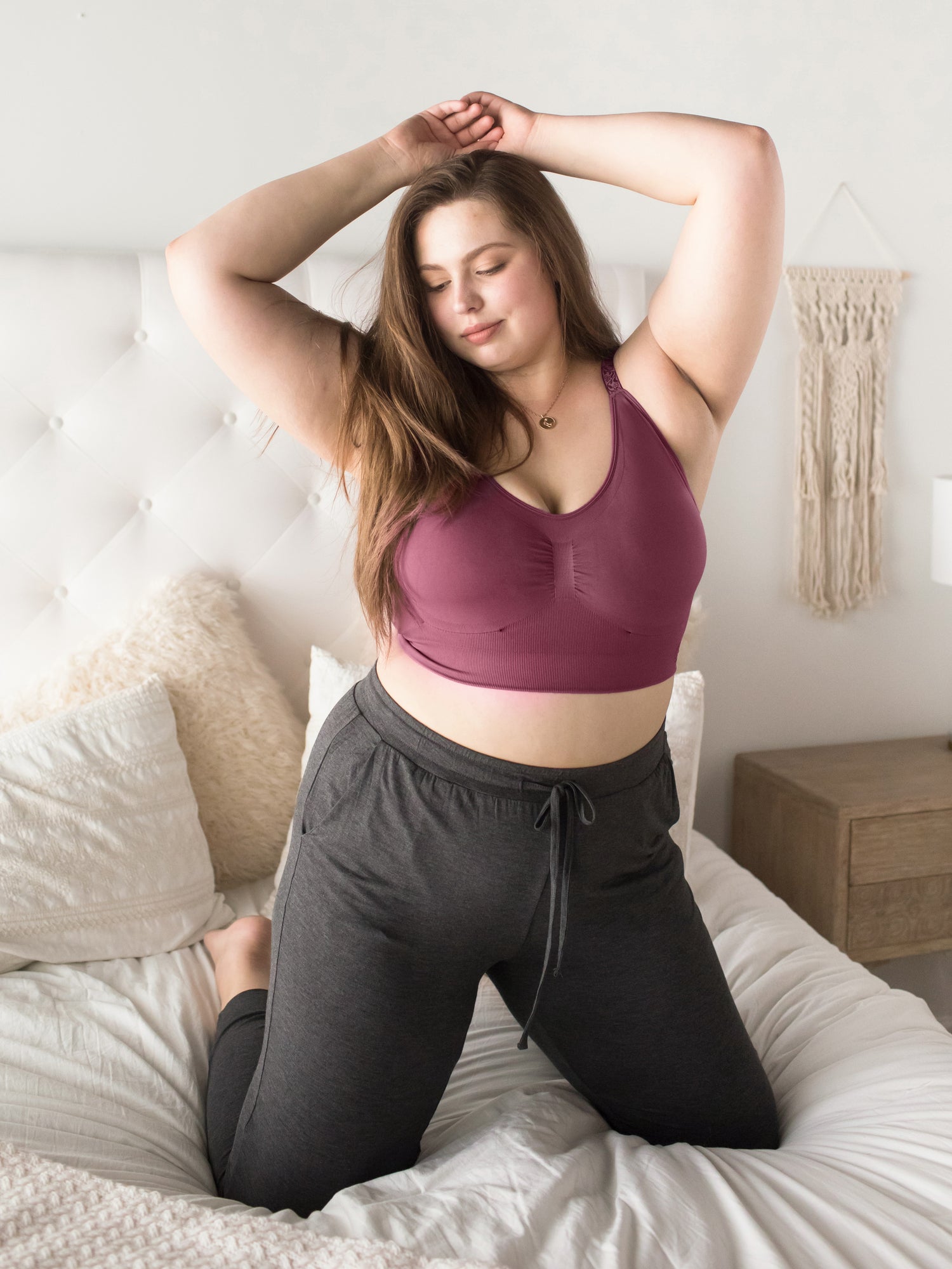 Model sitting on a bed wearing the Nellie Sublime® Wireless Bra in Fig