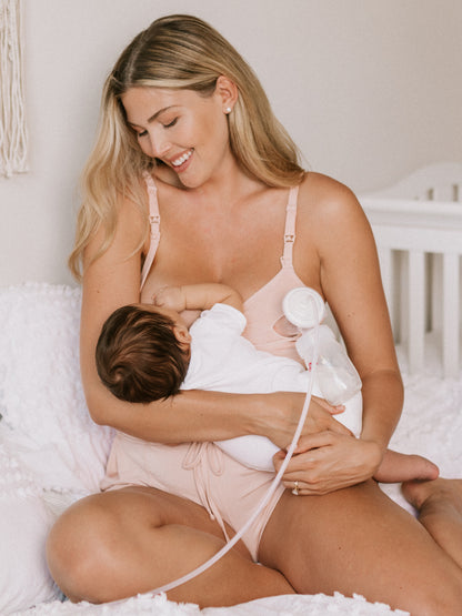 Model breastfeeding her baby while wearing the Sublime® Hands-Free Pumping & Nursing Bra in Pink Heather
