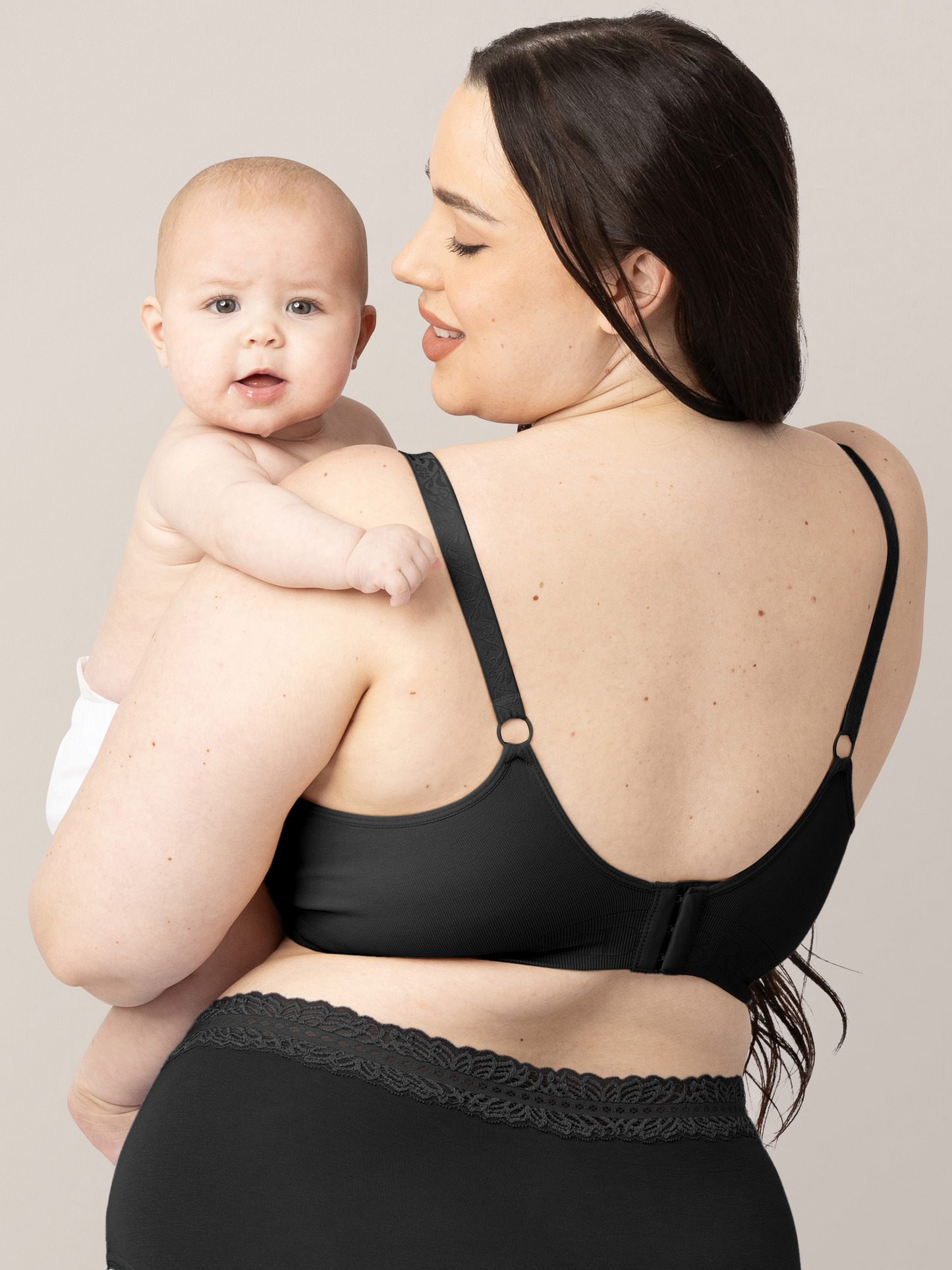 Back of a model wearing the Simply Sublime® Nursing Bra in Black holding her baby on her hip.