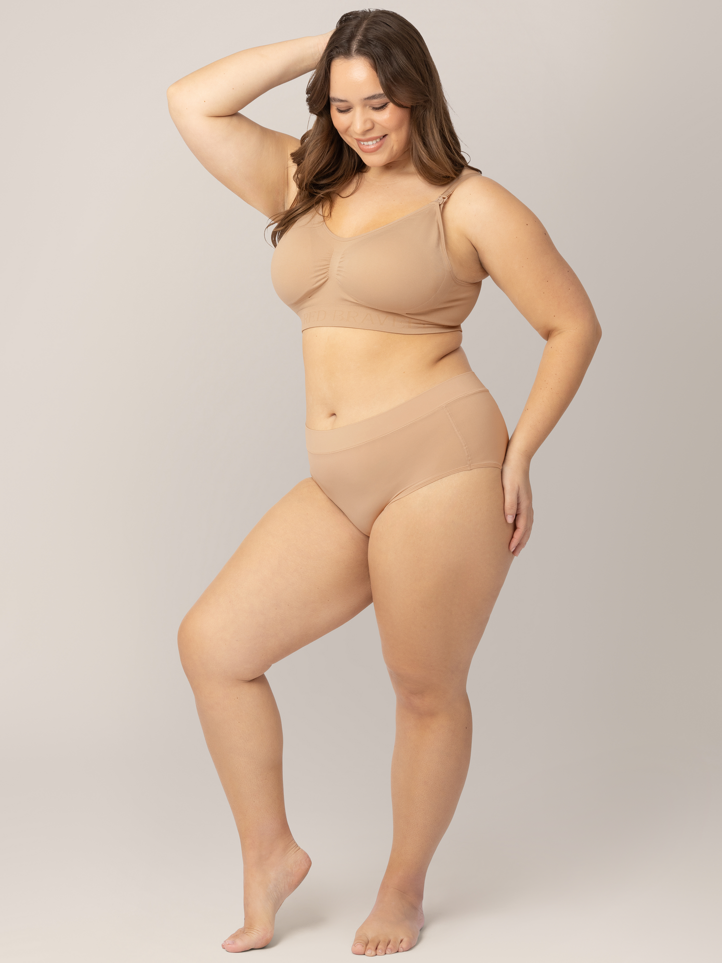 Busty model wearing the Grow with Me™ Maternity & Postpartum Brief in Beige with one hand on her hip and the back of her head.