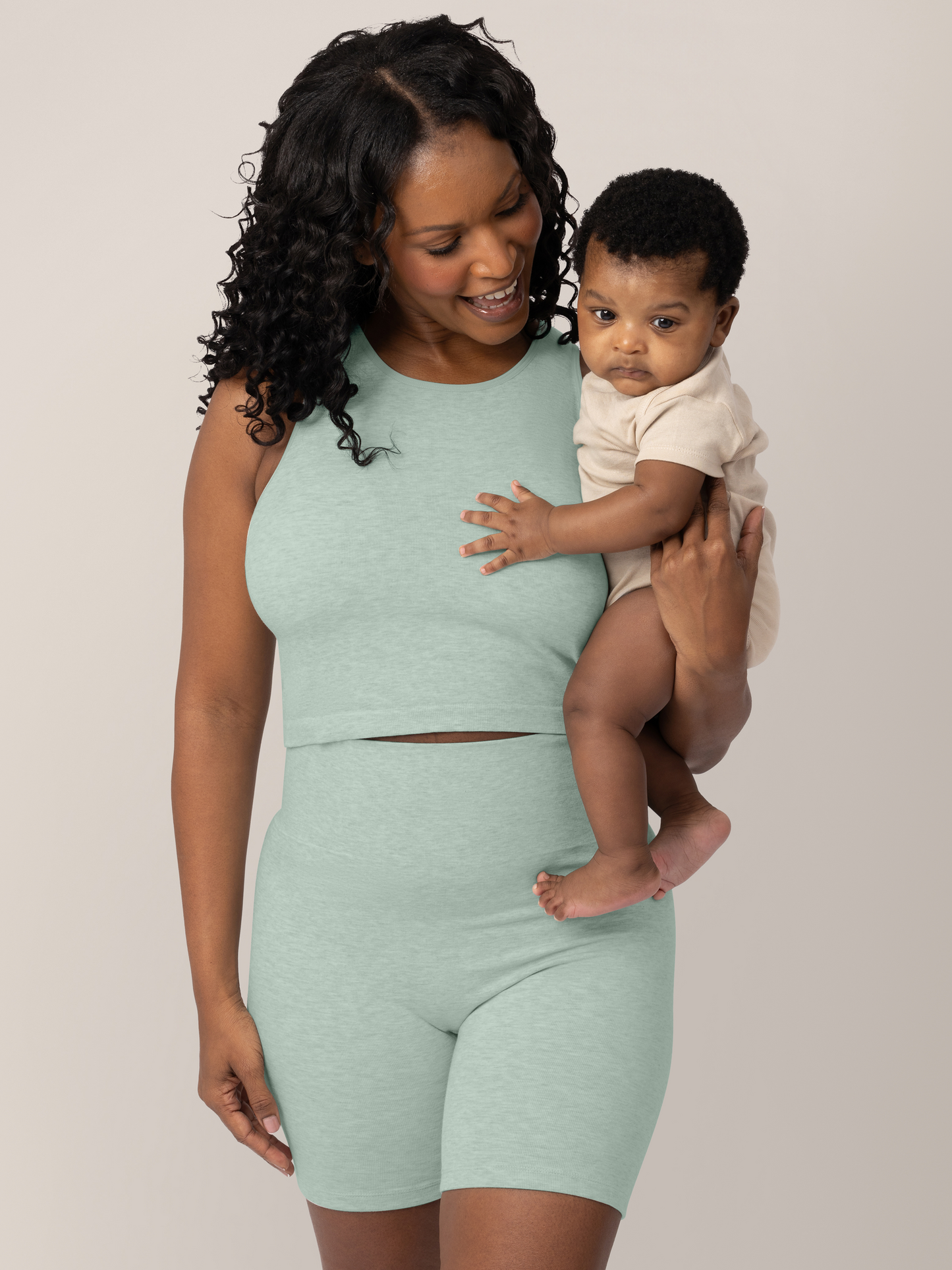 Front view of model holding baby and wearing the Sublime® Bamboo Maternity & Nursing Longline Bra in dusty blue green heather, paired with matching Sublime® Bamboo Maternity & Postpartum Bike Short. @model_info:Rashé is wearing a Small.