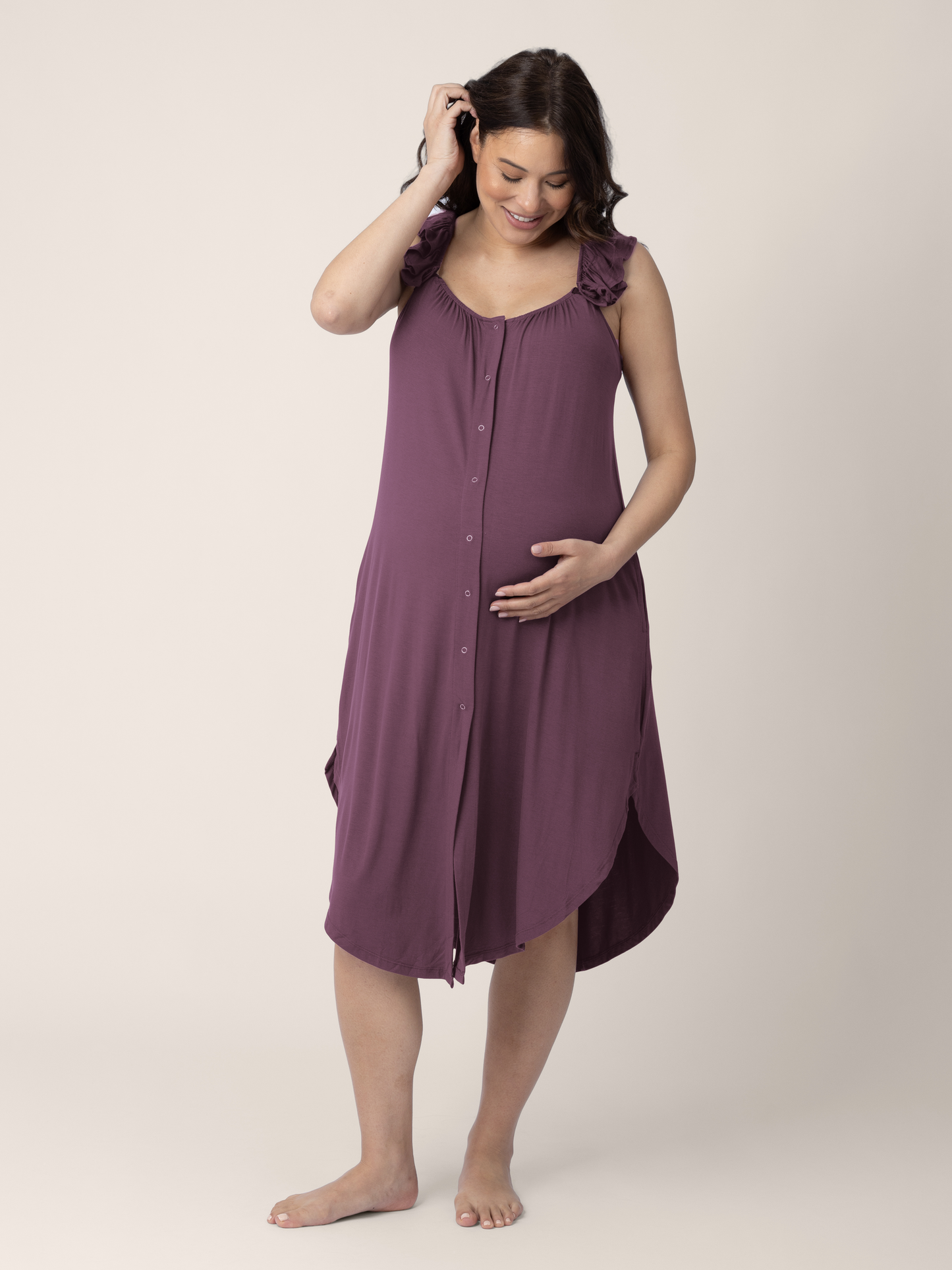 Model wearing the Ruffle Strap Labor & Delivery Gown in Burgundy Plum with her hand on her stomach. @model_info:Vanessa is 5'8" and wearing an XS/S.