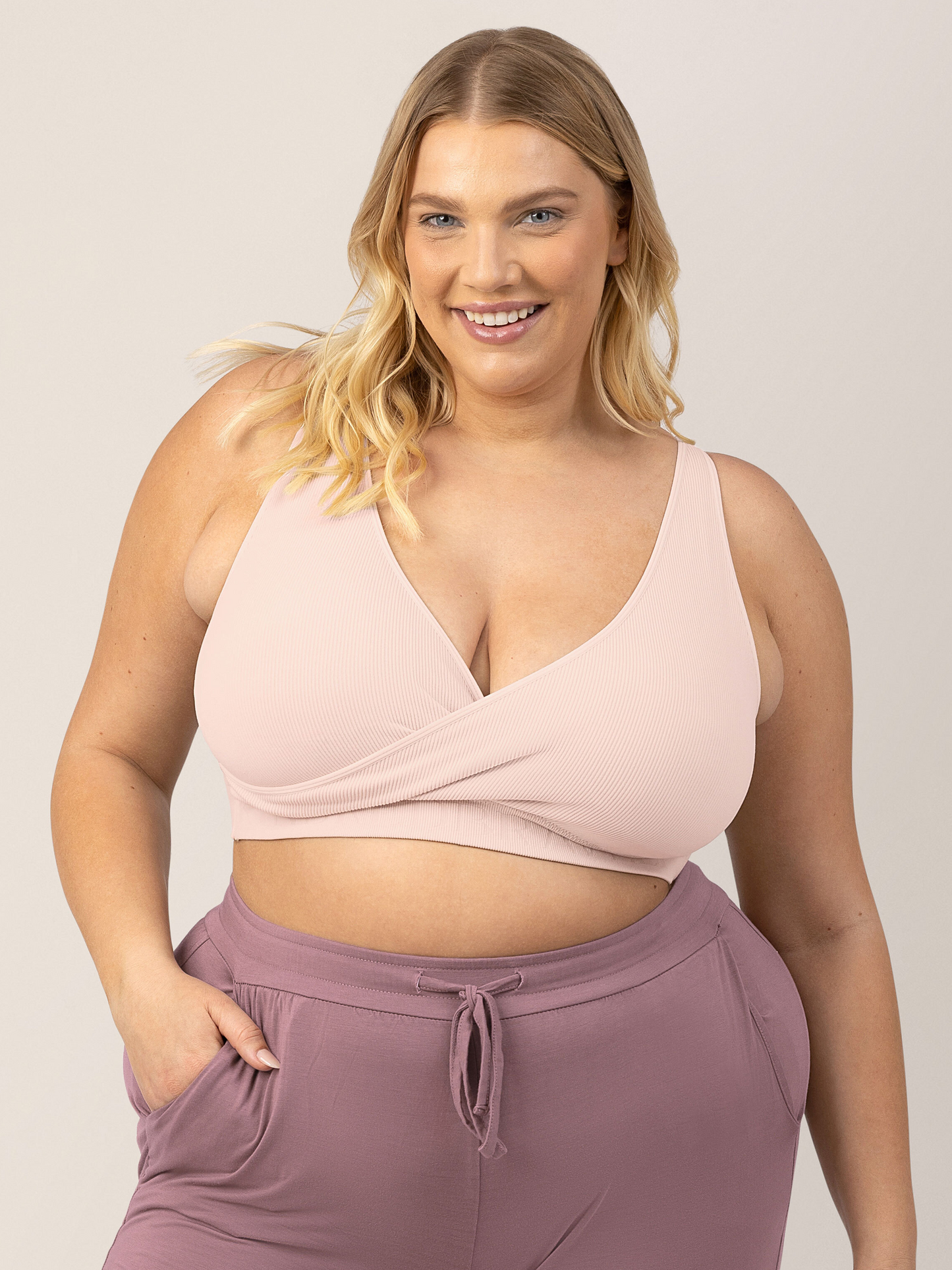 Busty Model wearing the Sublime® Adjustable Crossover Nursing & Lounge Bra in Soft Pink with her hand in her pocket. @model_info:Lauren is wearing an X-Large Busty.