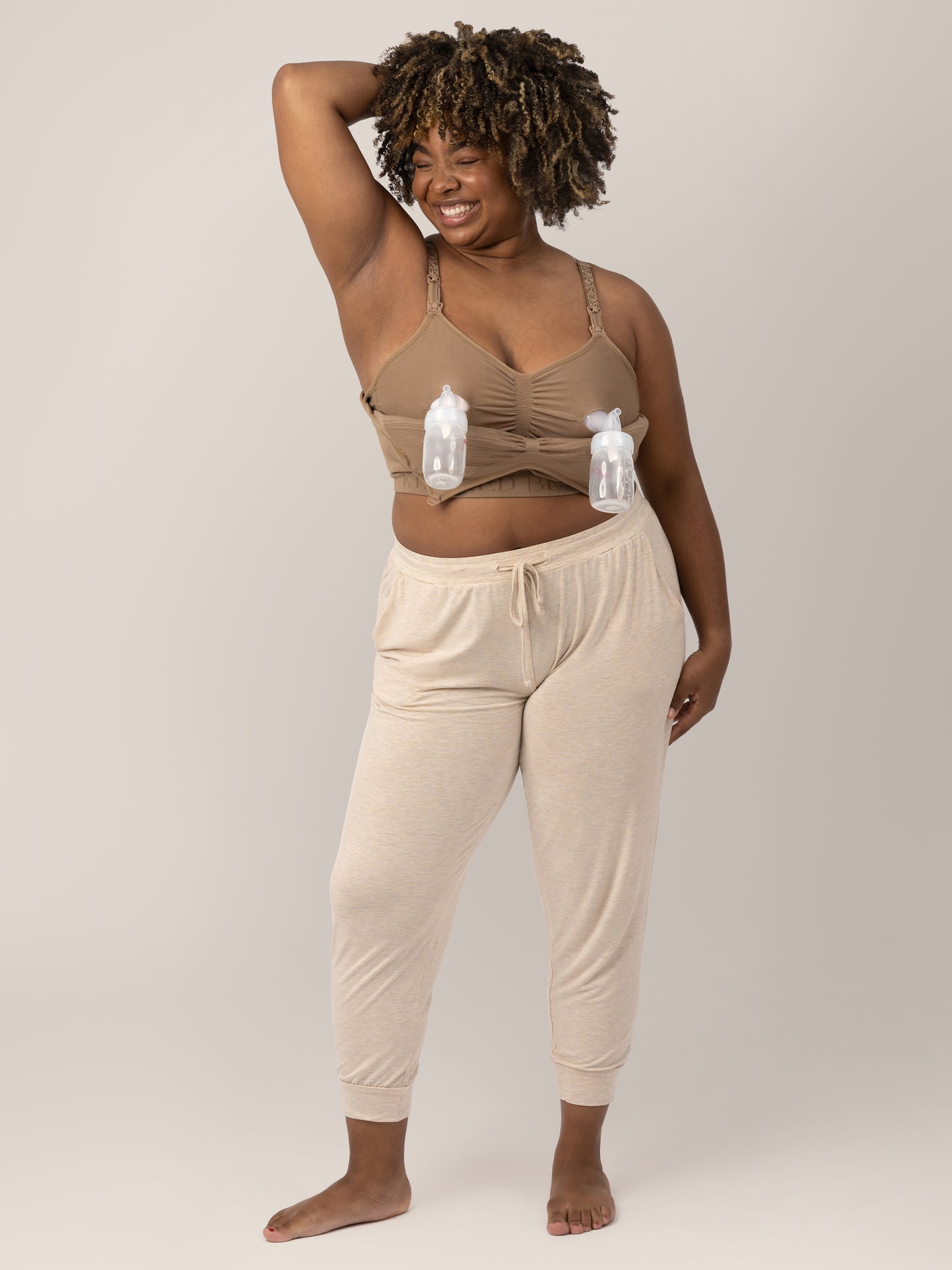 Model with one hand behind her head, wearing the Sublime® Hands-Free Pumping & Nursing Bra in Latte hooked up to two bottles