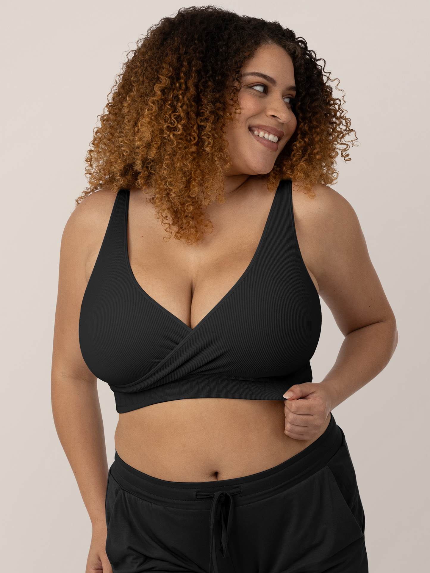 Model wearing the Sublime® Adjustable Crossover Nursing & Lounge Bra in Black smiling to the right. @model_info:Micah is wearing a Large Busty.