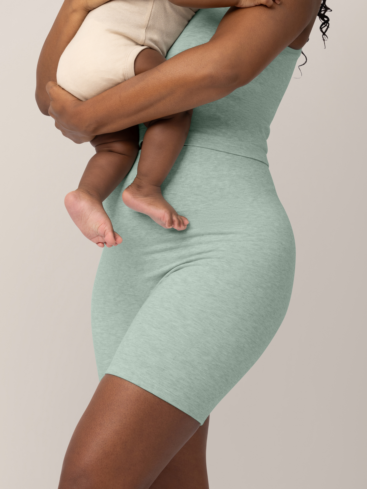 Close up 3/4 view of model holding baby and wearing the Sublime® Bamboo Maternity & Postpartum Bike Short in Dusty Blue Green Heather, paired with the matching Sublime® Bamboo Maternity & Nursing Longline Bra.