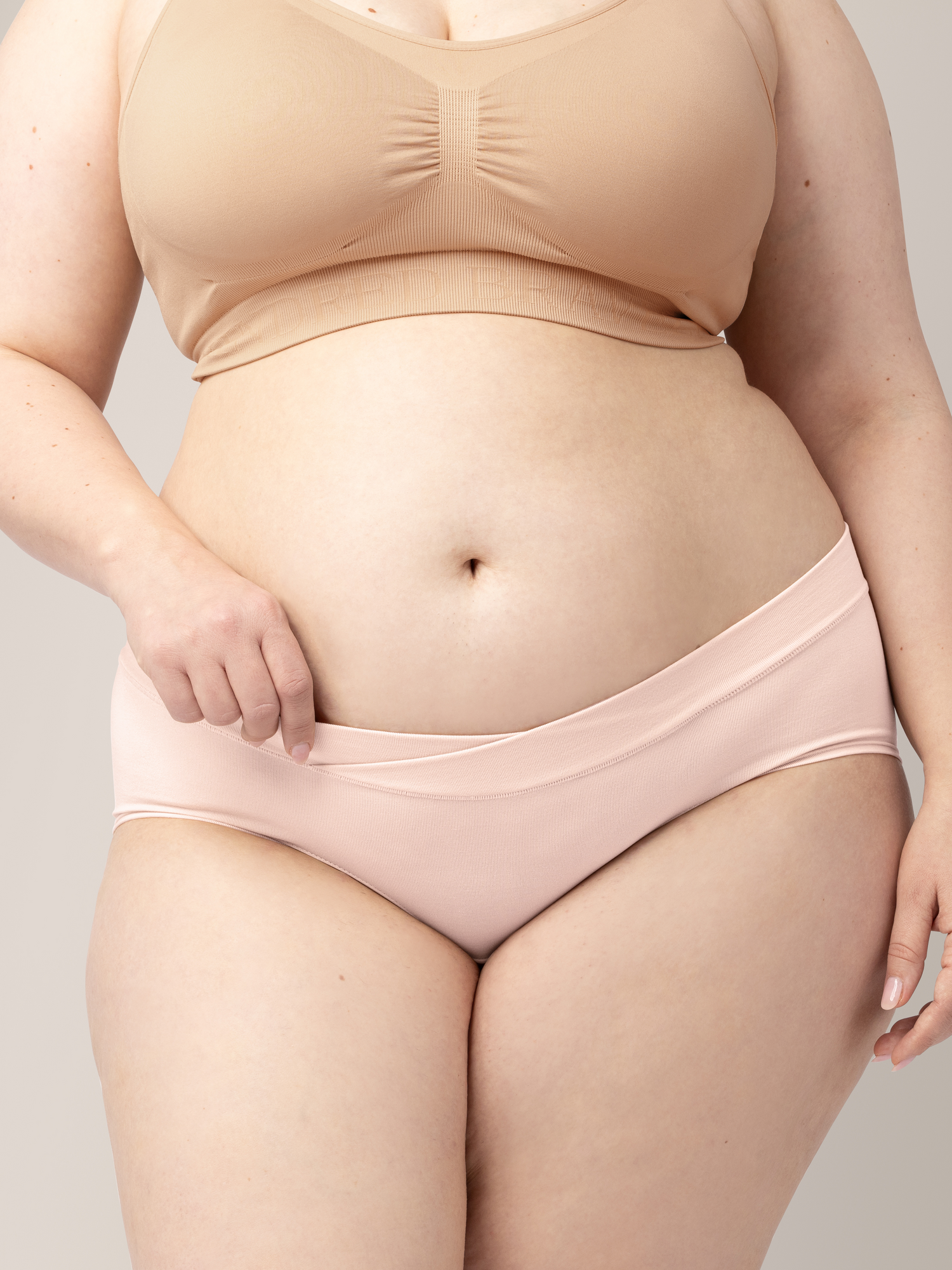Closeup of the Bamboo Maternity & Postpartum Hipster in Soft Pink with her hand on the waistband.