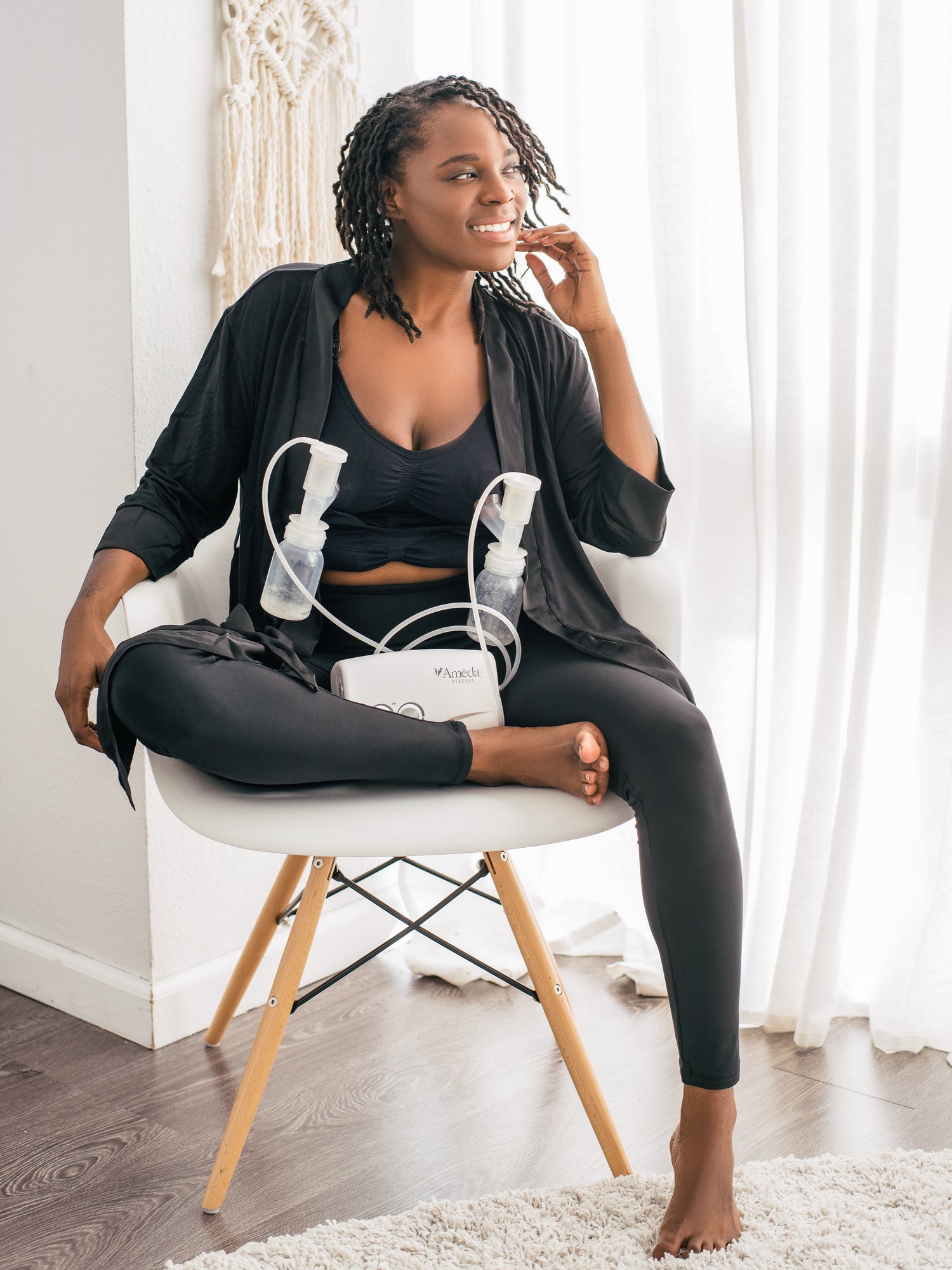 Model sitting in a chair hooked up to a pump while wearing the Sublime® Hands-Free Pumping & Nursing Bra in Black @model_info:Adrinne is wearing a Medium Regular.