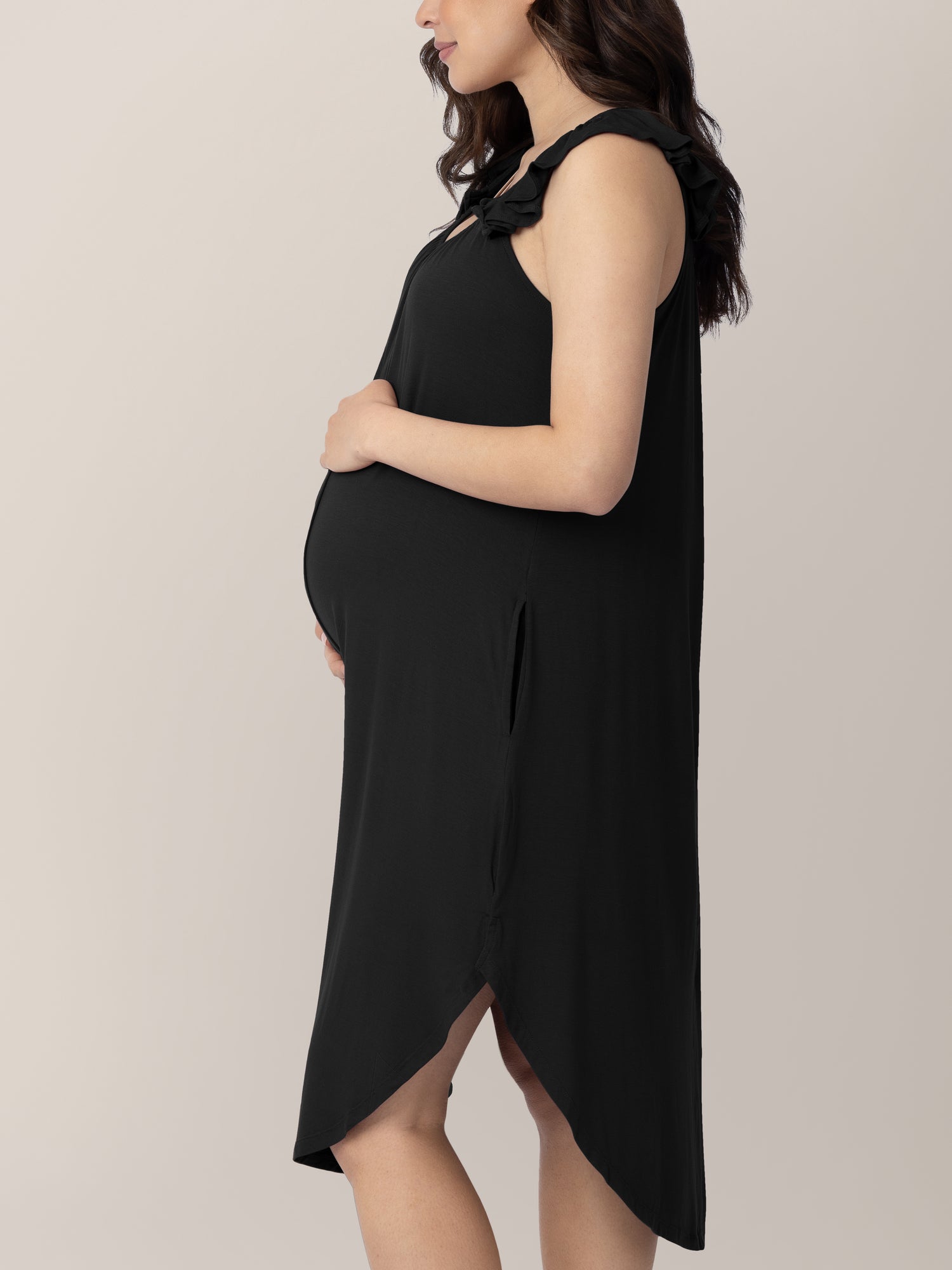 Side view of a pregnant model wearing the Ruffle Strap Labor & Delivery Gown in Black showing the pocket.