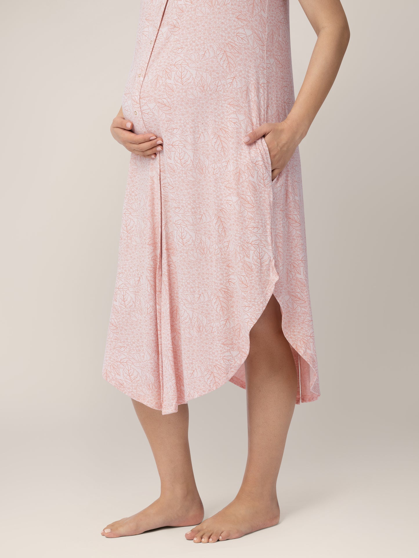 Closeup of the bottom half of a pregnant model wearing the Ruffle Strap Labor & Delivery Gown in Pink Hydrangea with her hand in her pocket.