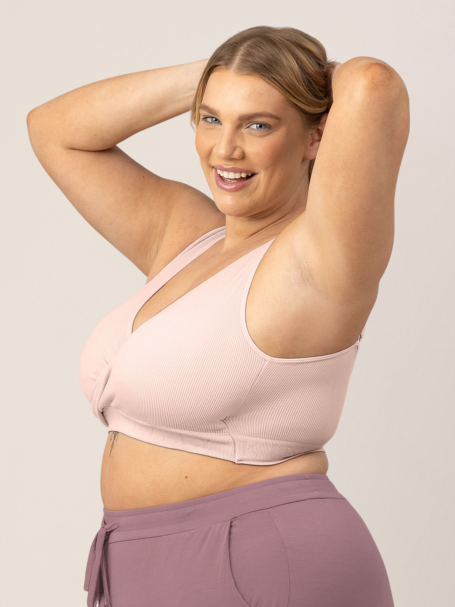 Busty model with her hands in her hair wearing the Sublime® Adjustable Crossover Nursing & Lounge Bra in Soft Pink