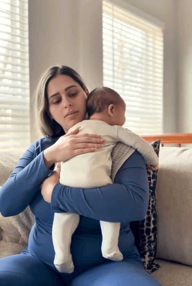 Rotating video of mother holding sleeping baby in a light filled home, sipping tea and greeting dog. 
