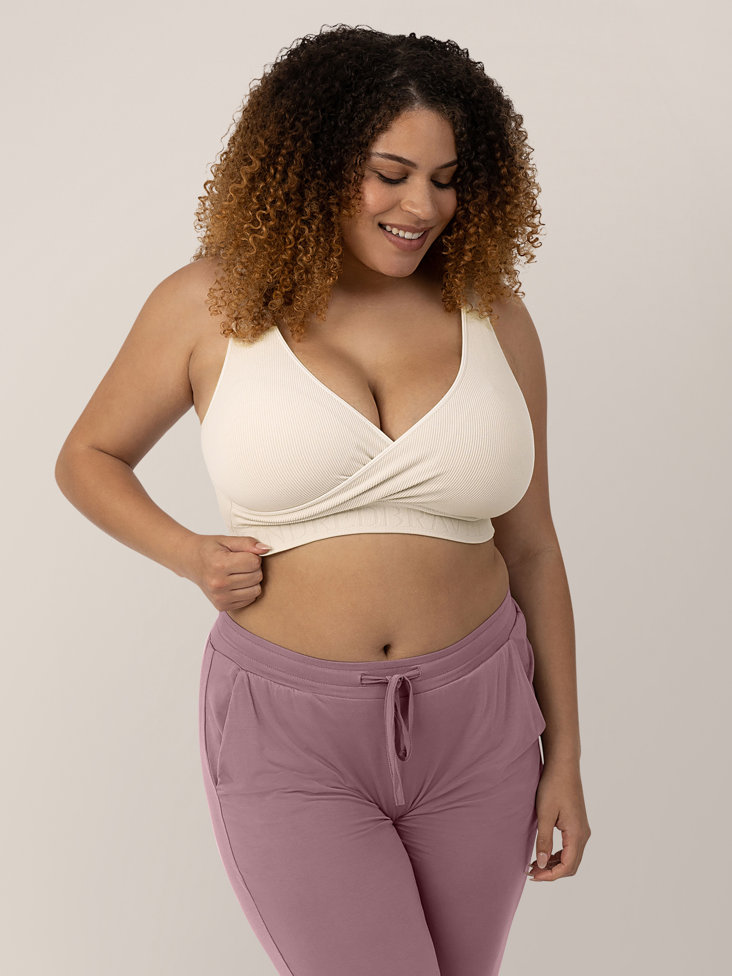 Busty model wearing the Sublime® Adjustable Crossover Nursing & Lounge Bra in Stone with her hand on her side. @model_info:Micah is wearing a Large Busty.