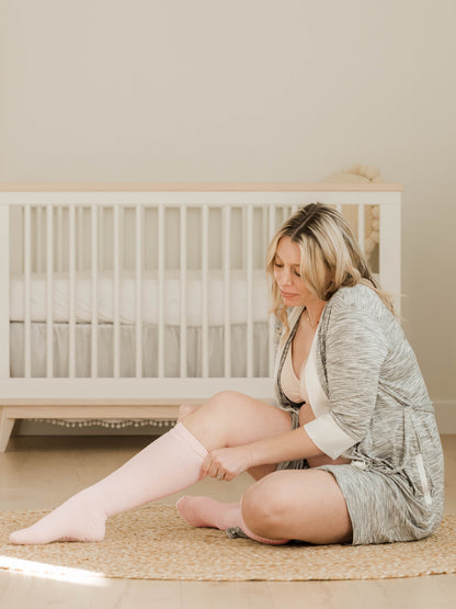 Model wearing the Premium Maternity Compression Socks sitting in front of a crib.