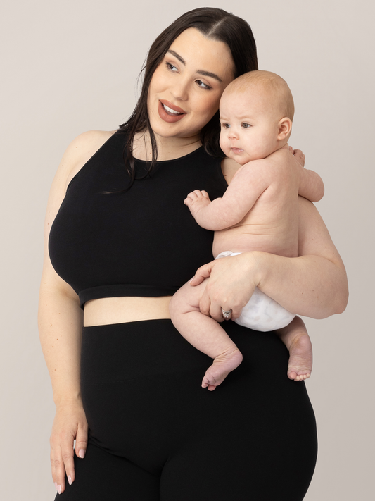 Model wearing the Sublime Bamboo Maternity & Nursing Longline Bra in Black and holding her infant. @model_info:Rachel is wearing an X-Large Busty.