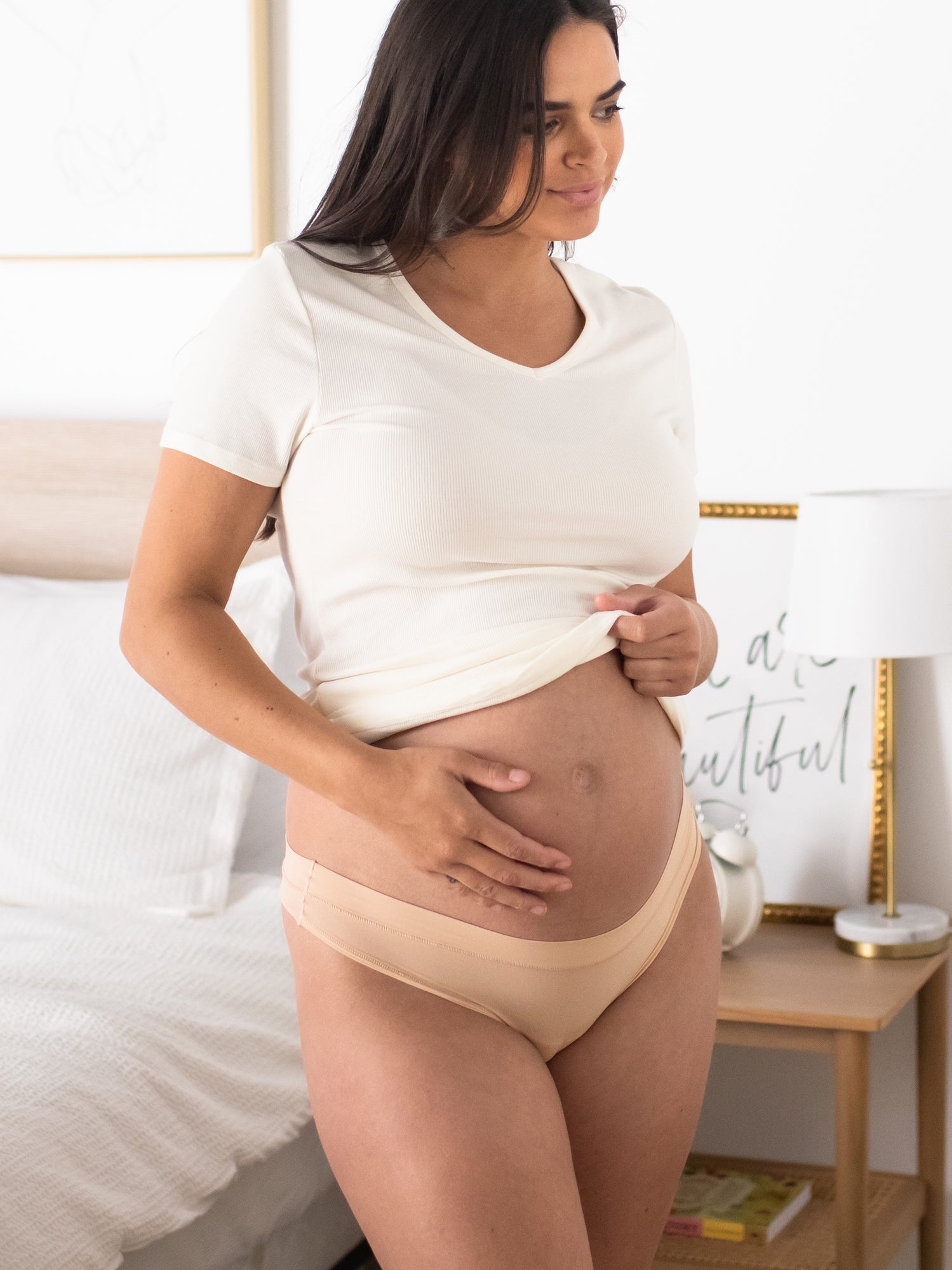 Model wearing the Grow with Me™ Maternity & Postpartum Thong in Beige with her hand on her belly bump. @model_info:Brooklyn is wearing a Small. 
